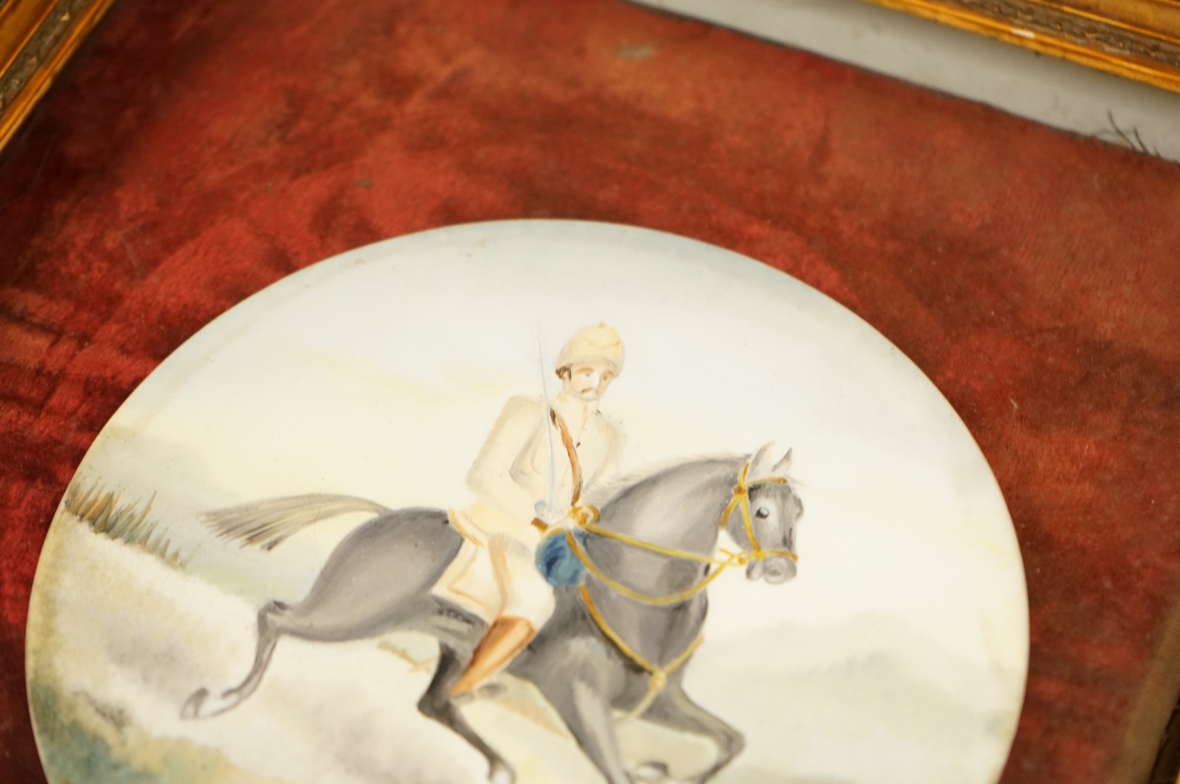 A pair of naive watercolours on circular porcelain panels, soldiers on horseback, framed, 15cm in diameter